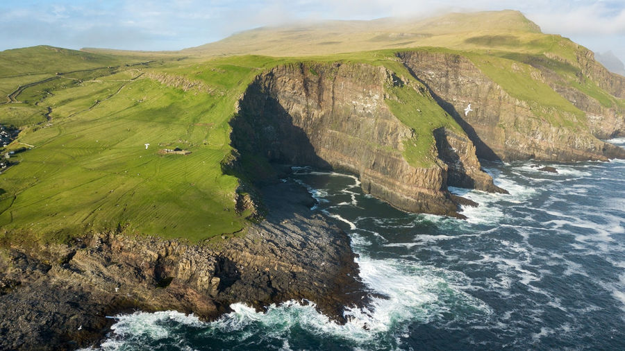 Scenic view of cliff by sea against cloudy sky