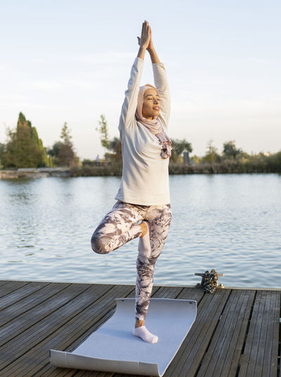 Full length of young woman doing yoga on lake