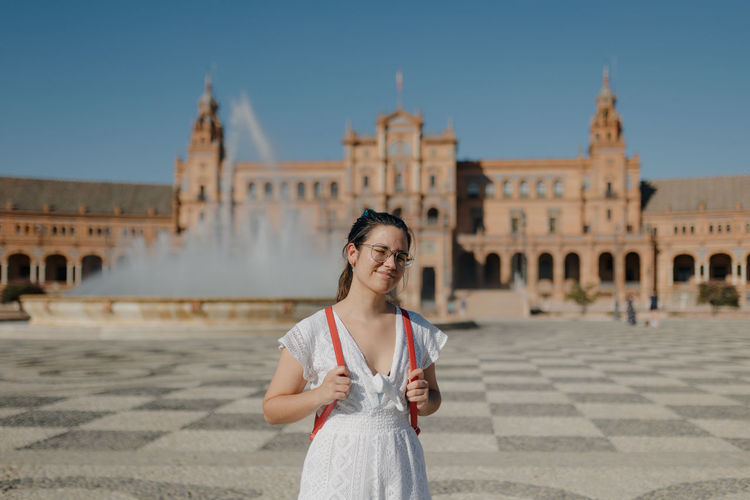 Young tourist woman wearing a white dress smiles at camera while standing in the plaza de españa