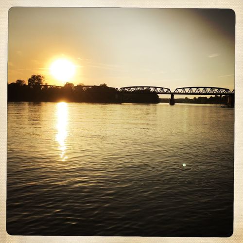 Bridge over calm river against sky during sunset