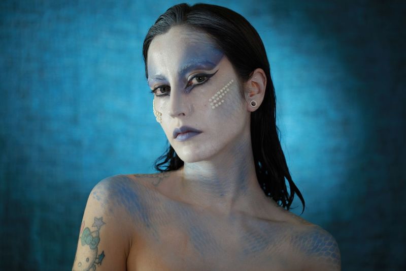 Portrait of young woman with face paint against blue background