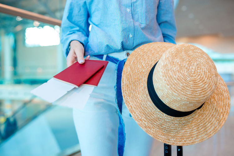 Midsection of woman holding passport and hat