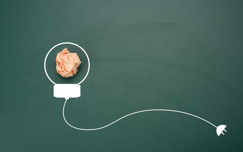 Crumpled sheet of paper on a green background, shape of a light bulb. energy saving concept, new 