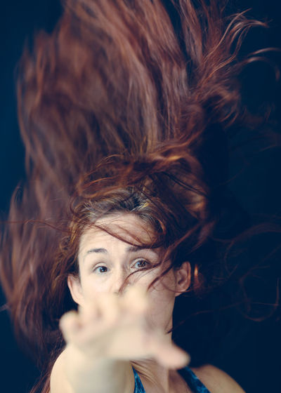 Close-up portrait of woman with tousled hair gesturing against black background
