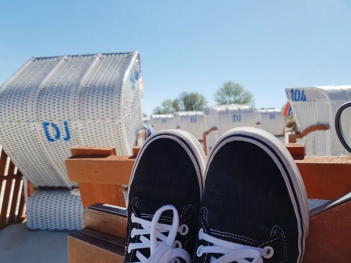 Close-up of shoes on seat against blue sky