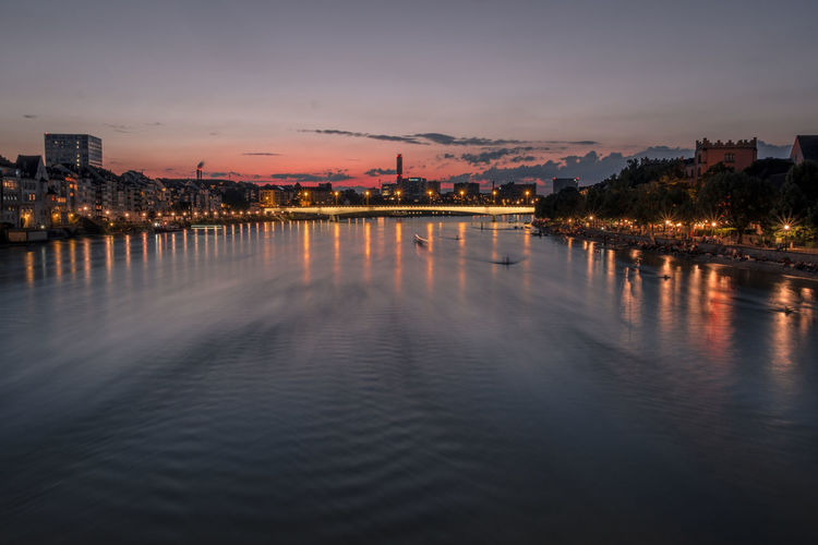 River by illuminated city against sky at sunset