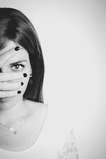 Close-up portrait of young woman covering face against white background