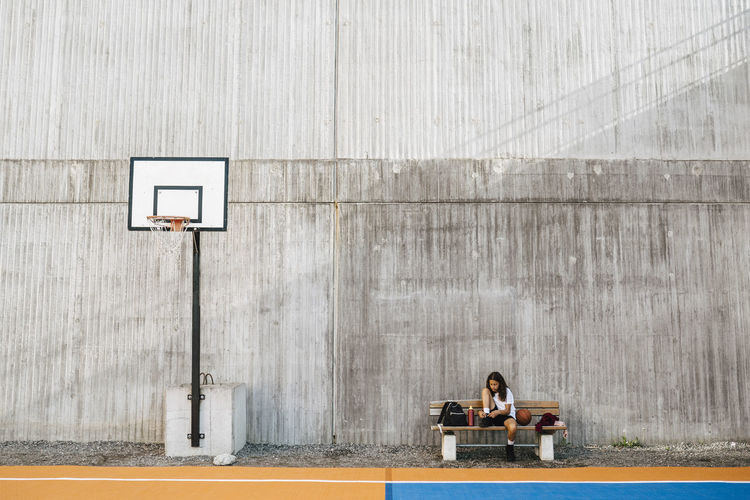 Girl tying shoelace while sitting on bench at basketball court