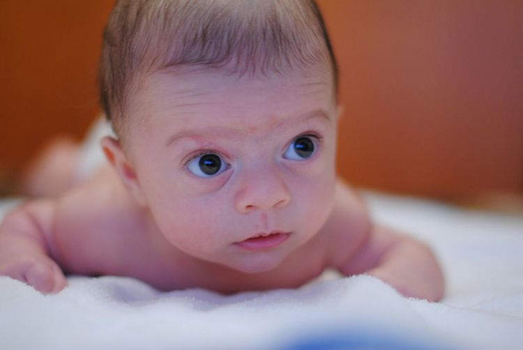 Close-up of shirtless baby looking away while lying on bed