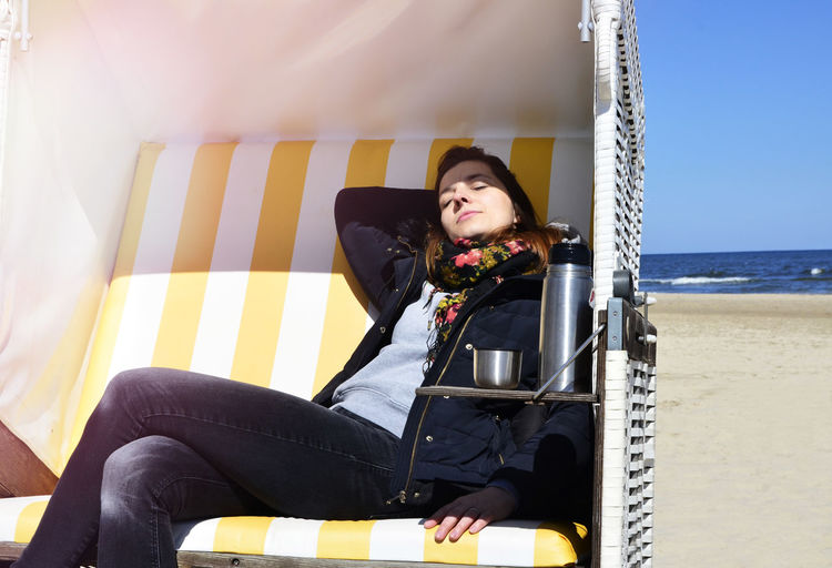 Young woman resting in yellow hooded beach chair on sea shore during sunny day
