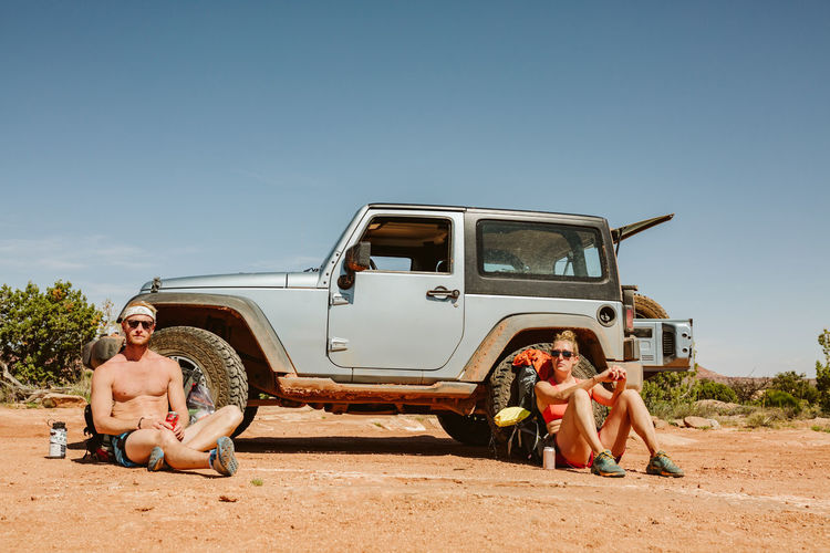 Portrait of two straight faced hikers sitting in front of jeep