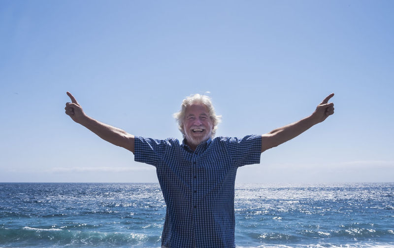Portrait of smiling senior man with arms outstretched standing at beach