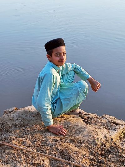Portrait of boy sitting on rock by lake