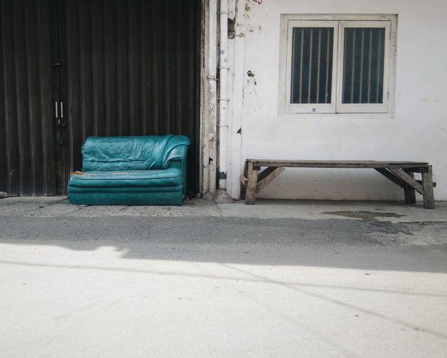 Old sofa by bench against building