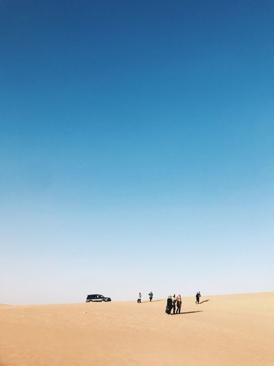 People on desert against clear blue sky