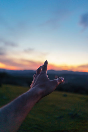 Cropped hand against sky during sunset