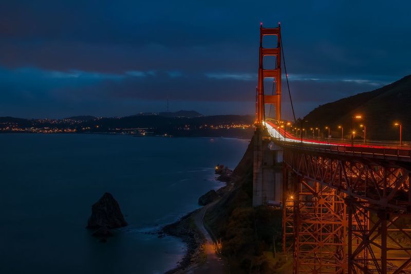 Golden gate bridge by sea against cloudy sky in city at night