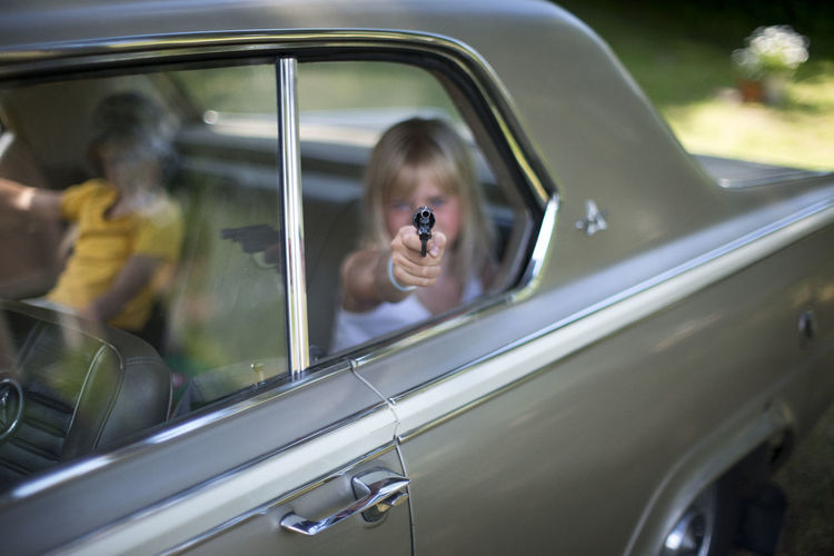A girl with a toy gun in the rearseat of a car