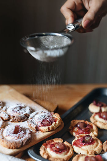 Cropped hand of woman dusting powdered sugar on cookies with strainer on table
