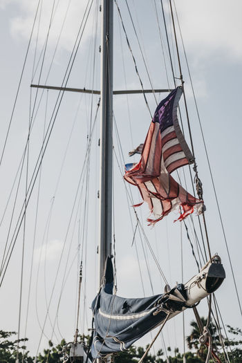 Low angle view of torn american flag waving on boat against sky