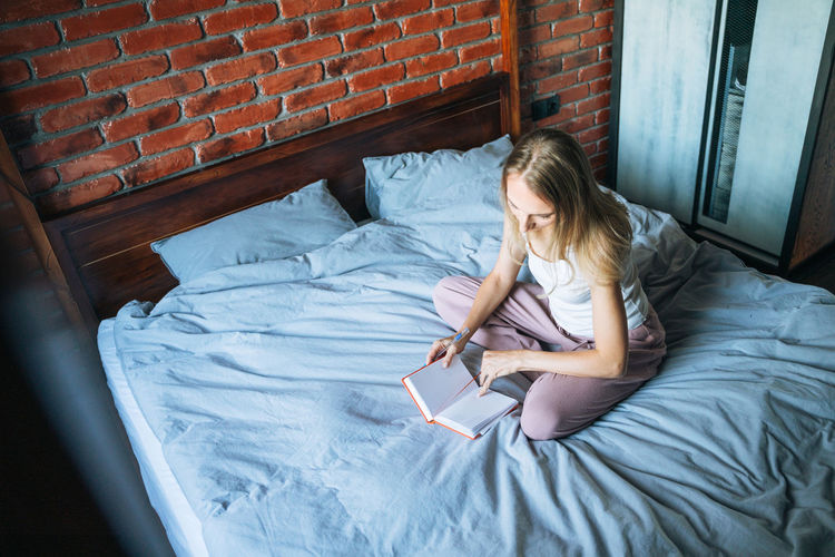 Young adult woman forty years writes notes in planner on bed at home