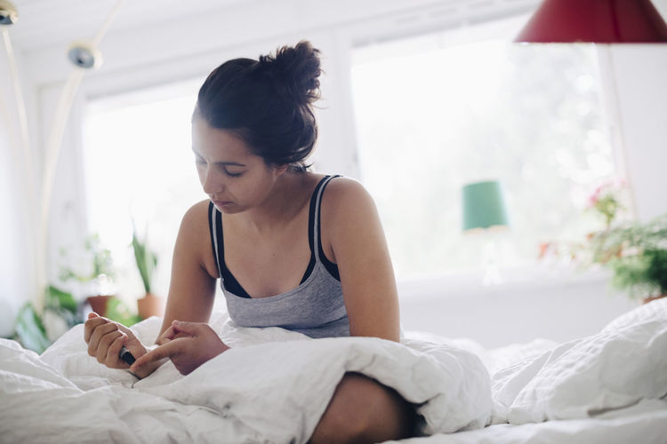 Woman checking blood sugar level while sitting on bed