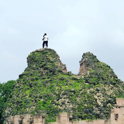 Low angle view of couple standing on rock against sky