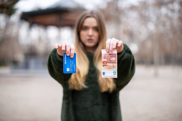 Portrait of woman holding credit card and money while standing outdoors