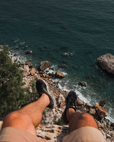 Low section of man relaxing on rock by sea
