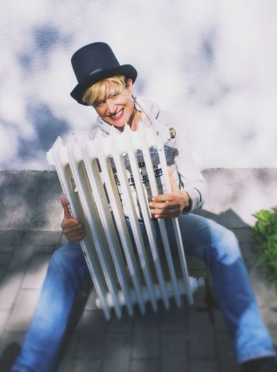 High angle portrait of woman holding radiator while sitting on footpath