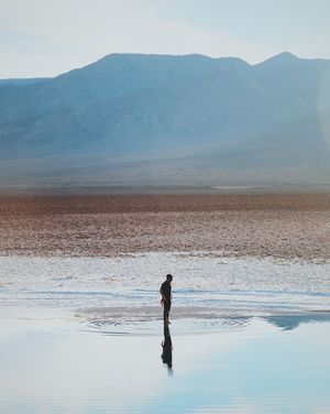 Man standing by reflection in lake against mountain