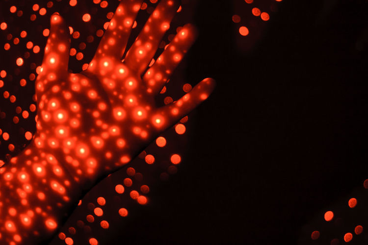 Defocused image of illuminated lights on human hand over black background