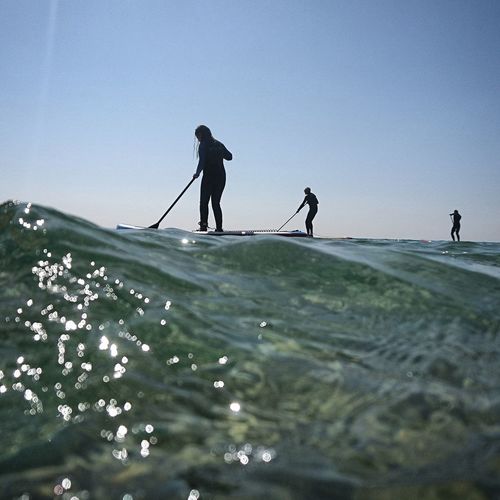People on paddleboarding in sea against sky