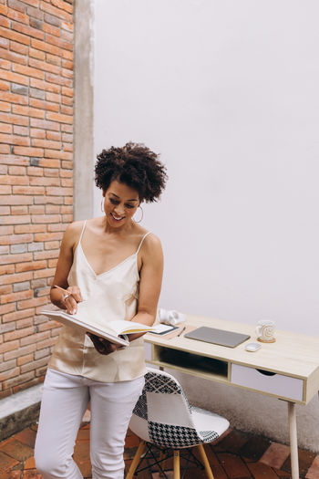 Black woman reading and writing notes in a notebook standing next to a workstation