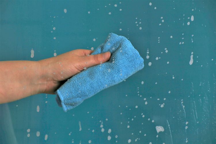 Cropped hand cleaning wet glass window with rag against turquoise background