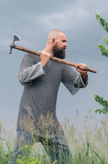 Side view of man in medieval viking clothing. metal helmet and chain mail. threatens with ax.