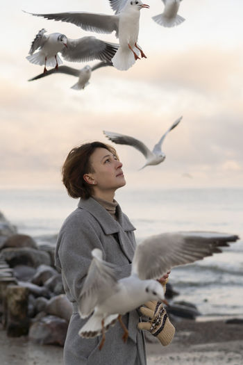 Thoughtful woman amidst flying seagulls at beach