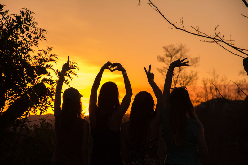 Silhouette of women gesturing against sky during sunset