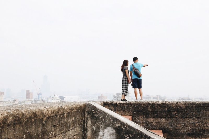 Rear view of couple standing on wall in city against clear sky