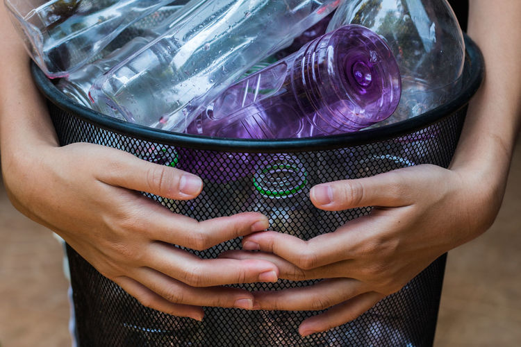 Midsection of woman holding garbage can of bottles