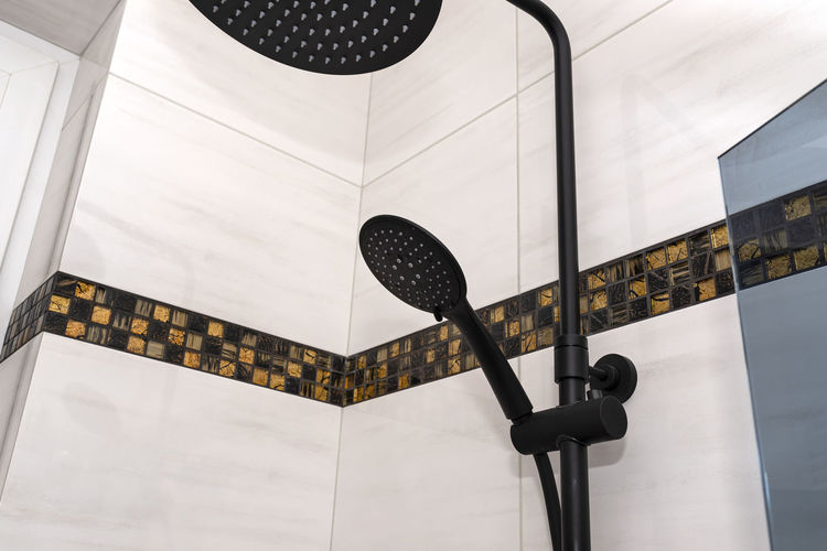 A modern, black metal shower with small and large rain shower, placed on tiles.