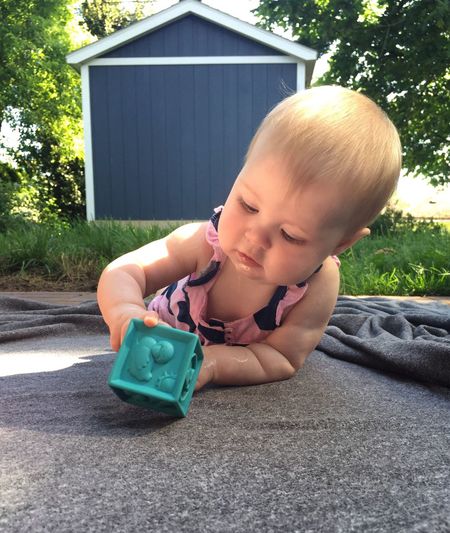 Close-up of baby girl playing with toy while lying on blanket in yard