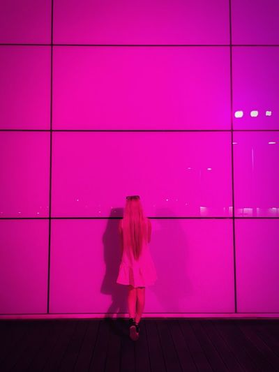 Rear view of woman standing by illuminated pink wall at night