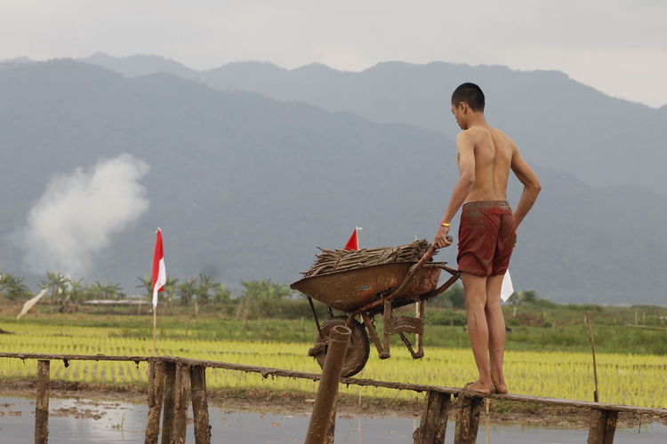 Man carrying firewood in wheelbarrow on narrow footbridge