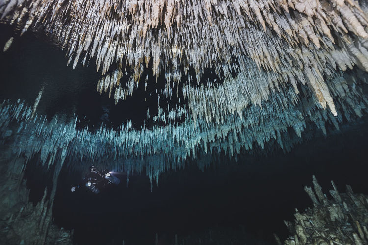 Low angle view of man scuba diving below stalactites in sea