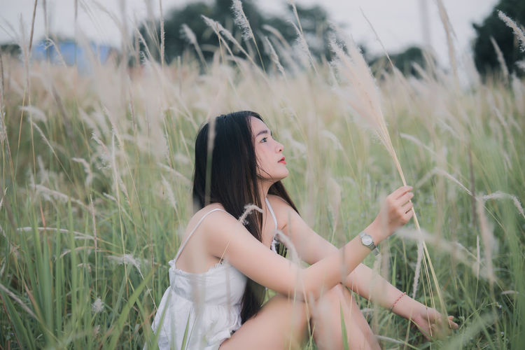Side view of young woman sitting amidst grass on land