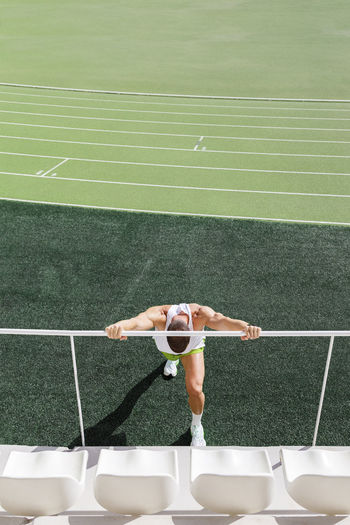 Athlete doing warm exercise by railing on sports field