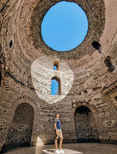 Man standing inside ancient roman building with natural light shining on him through circular roof.