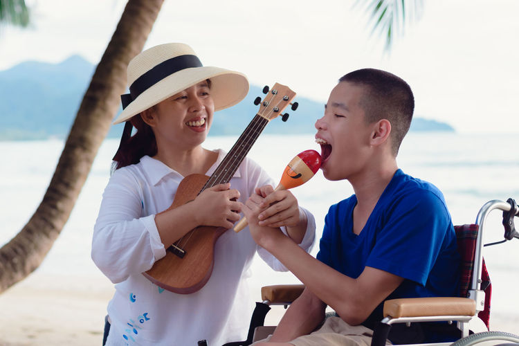 Cheerful mother holding ukulele sitting with boy at beach