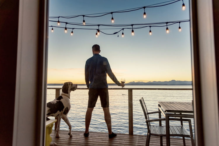 Man with dog standing in boat deck over sea against sky